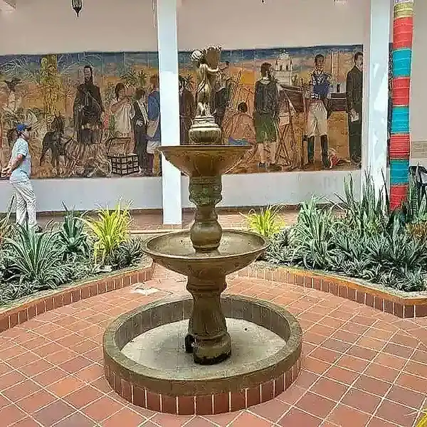 Una fuente en el centro de un patio con mural y plantas decorativas.