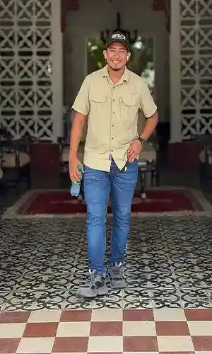 Hombre sonriendo en un lugar decorado con paredes de madera y plantas.