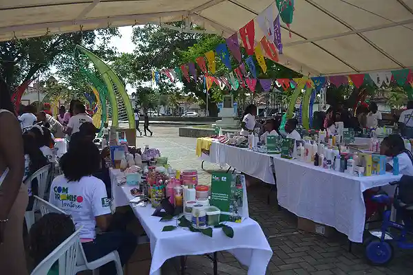Gremios 3 Personas participando en una feria bajo carpa, exhibiendo productos artesanales y locales.